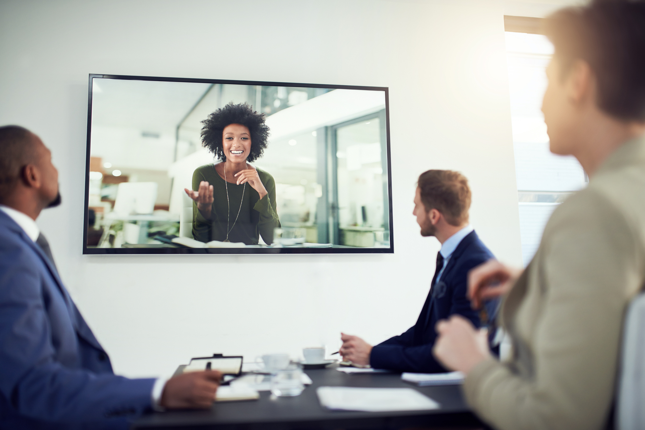 Kollegen im Büro besprechen sich mit Kollegin auf großem Monitor